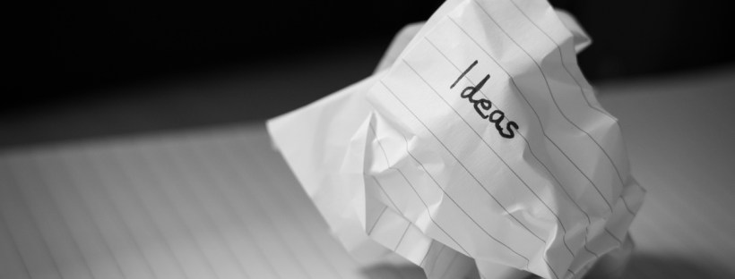 The word ideas is written on a crumpled piece of paper. It's sitting atop a flat sheet of paper, and the background is dark.